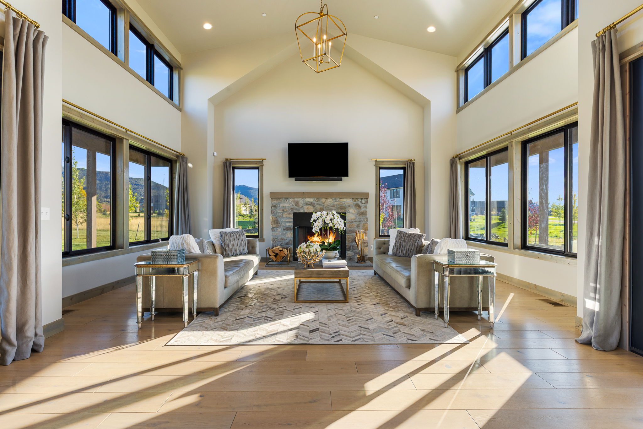 Bozeman luxury home great room at 58 Waylon Way in Home 40 featuring vaulted ceilings, expansive Andersen windows, stone fireplace, and mountain views through panoramic glass.